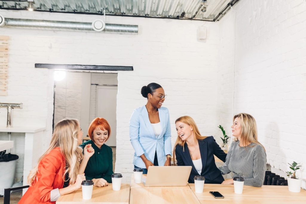 Happy African business woman, group leader celebrating success with female members of her team, being overjoyed, clapping hands with the others at meeting.